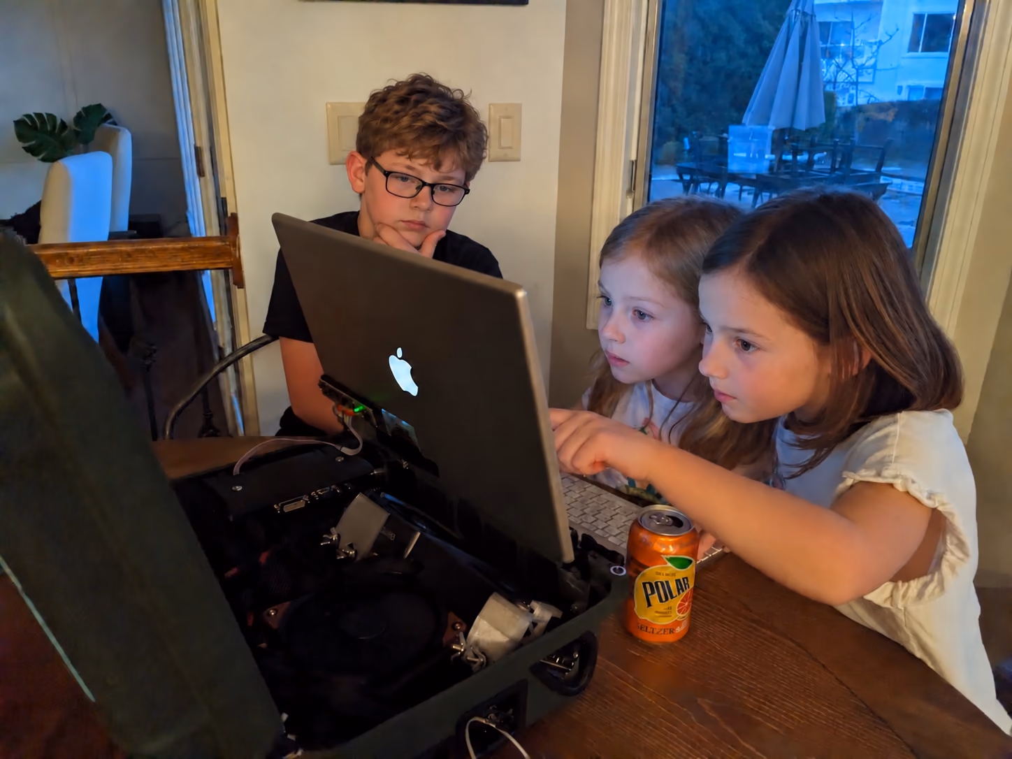 Three young people playing together on a portable PC built with a repurposed MacBook screen. Faces digitally altered.